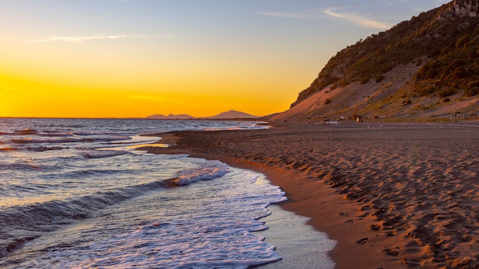 A beach with waves at sunset, a distant mountain, and a clear sky.