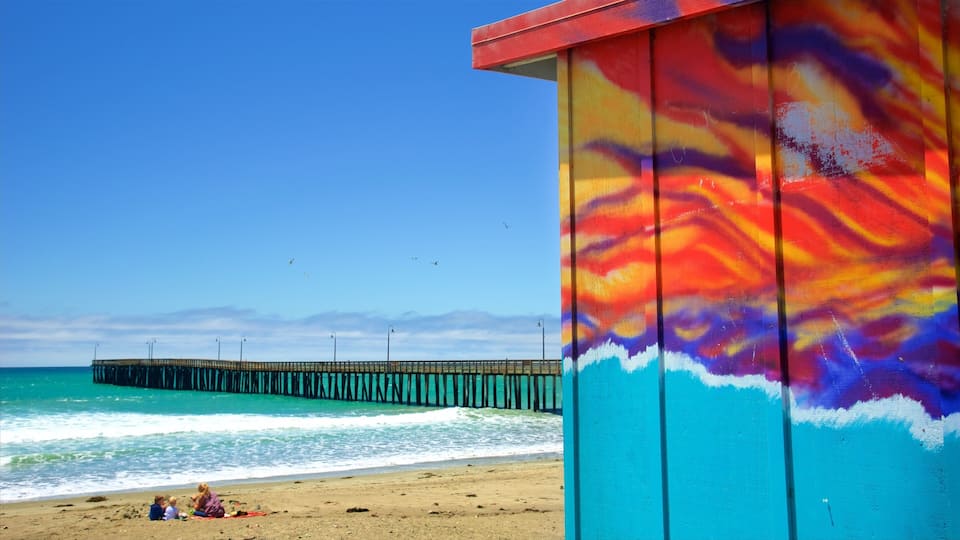 A colorful pier extending into turquoise waters, a sandy beach with people, and a clear blue sky.