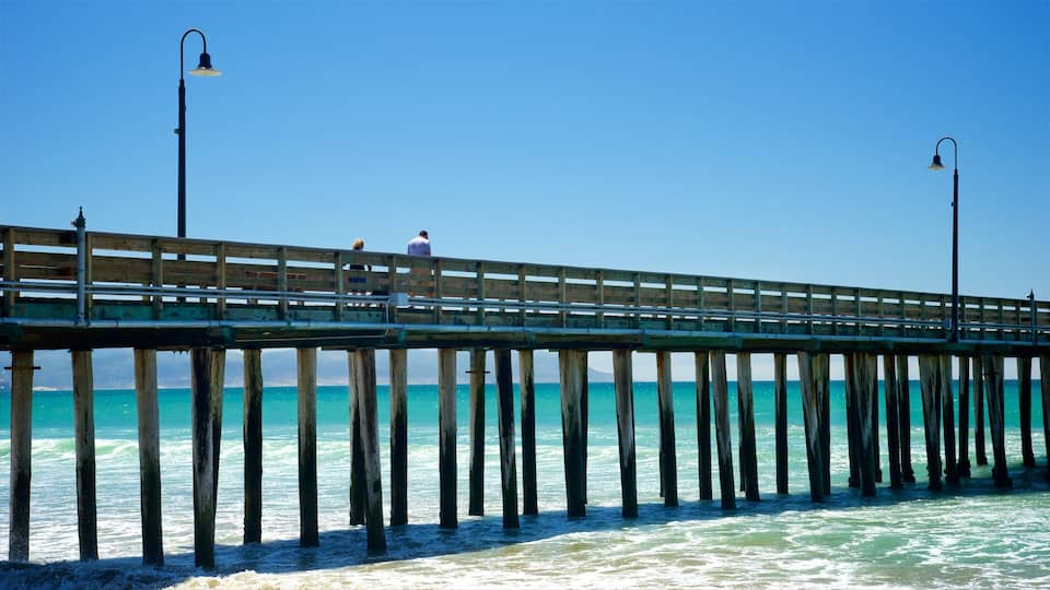 A wooden pier with railings and street lamps, extending into a turquoise sea.