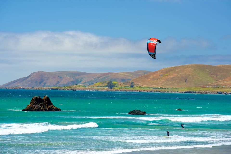 A coastal landscape with clear turquoise waters, rocky outcrops, and distant hills.