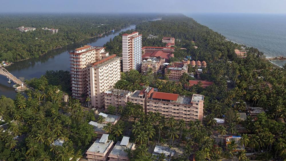 Aerial view of tall buildings and lush greenery meet the ocean's edge, a bridge arching over the tranquil river, Kollam, Kerala, India.