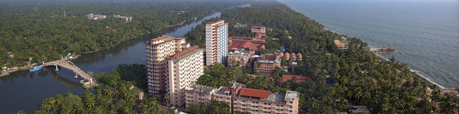 Aerial view of tall buildings and lush greenery meet the ocean's edge, a bridge arching over the tranquil river, Kollam, Kerala, India.