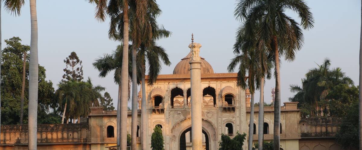 A historical building with a dome and arches, surrounded by palm trees.