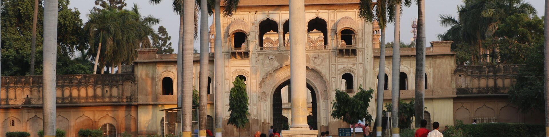 A historical building with a dome and arches, surrounded by palm trees.