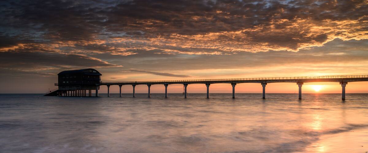 A pier extending into the water with a sunset in the background.