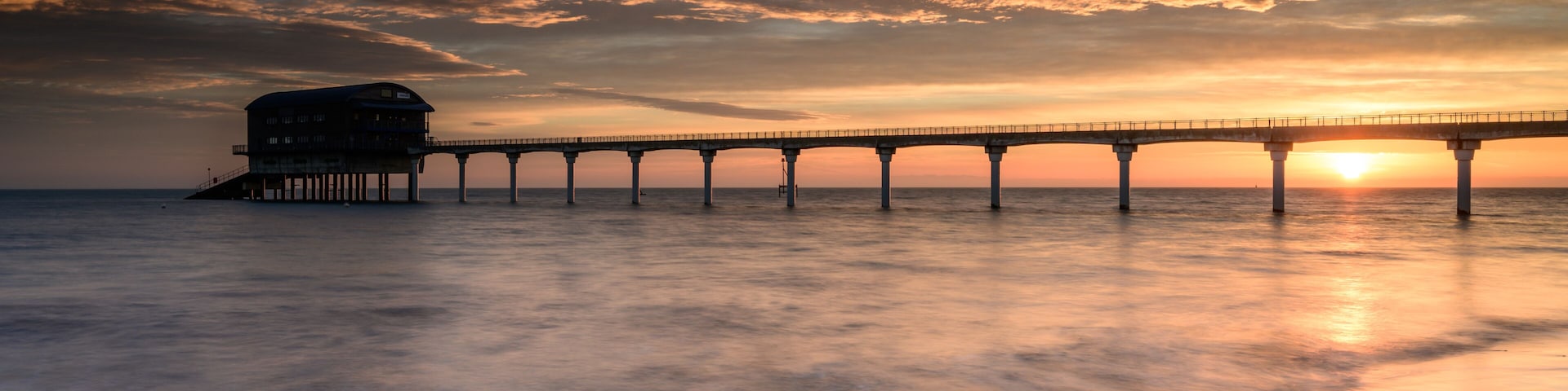 A pier extending into the water with a sunset in the background.