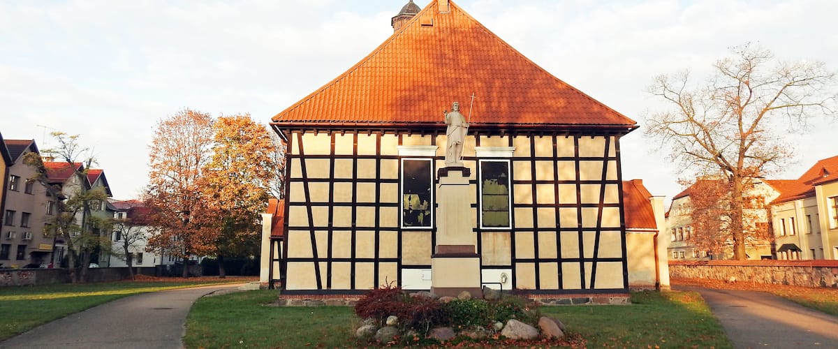 A half-timbered house with a red-tiled roof and a statue in front.