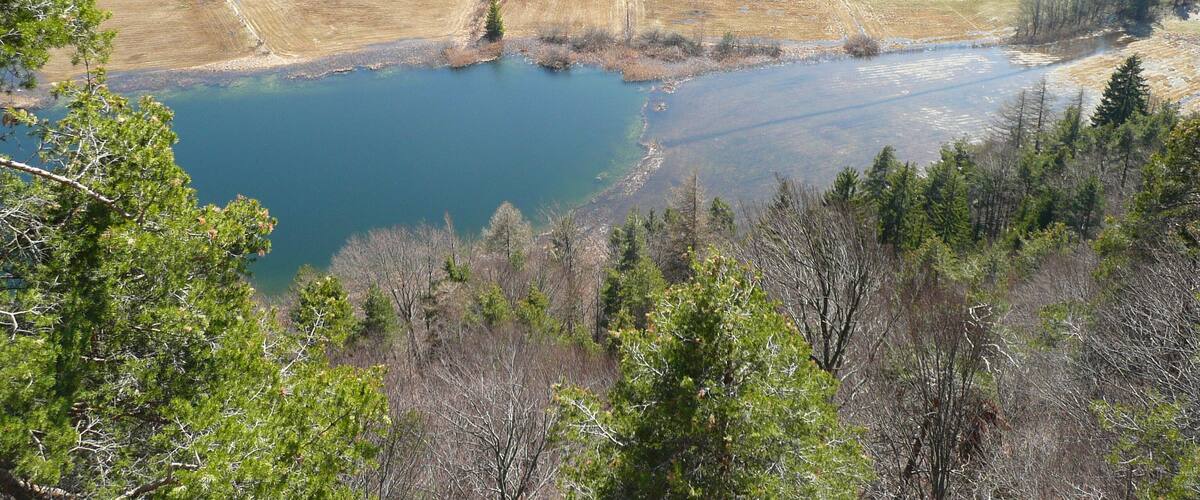A lake surrounded by forested hills and scattered buildings.