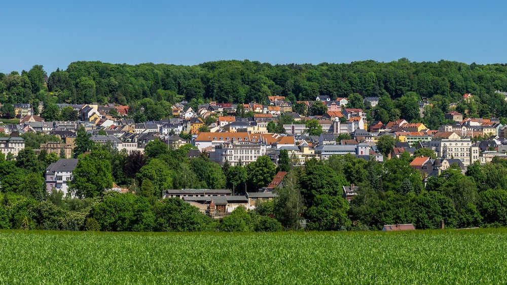 A town nestled in a valley with a prominent church tower, surrounded by lush greenery and fields.
