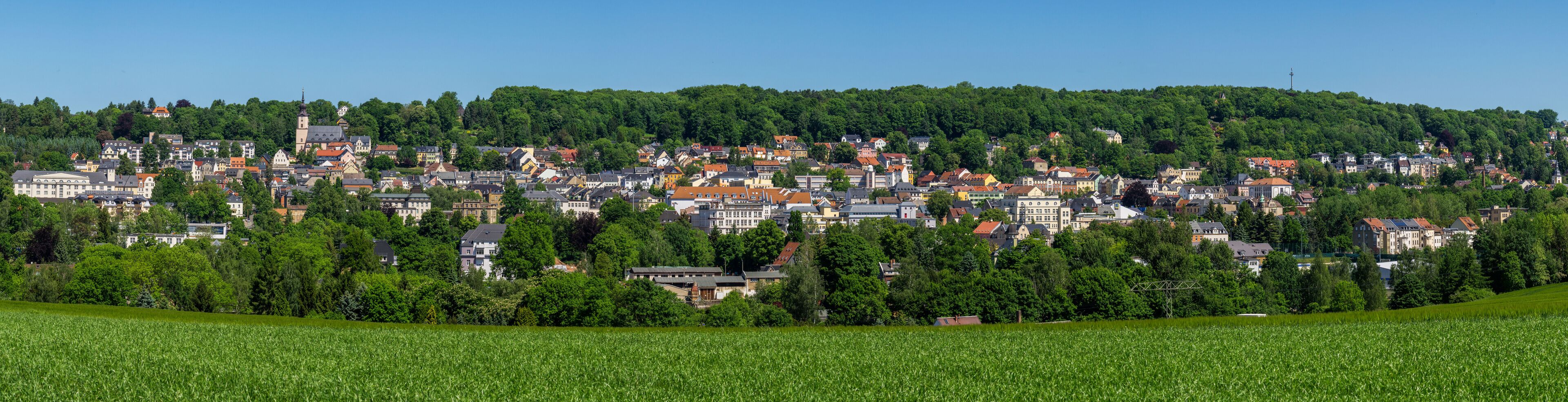 A town nestled in a valley with a prominent church tower, surrounded by lush greenery and fields.