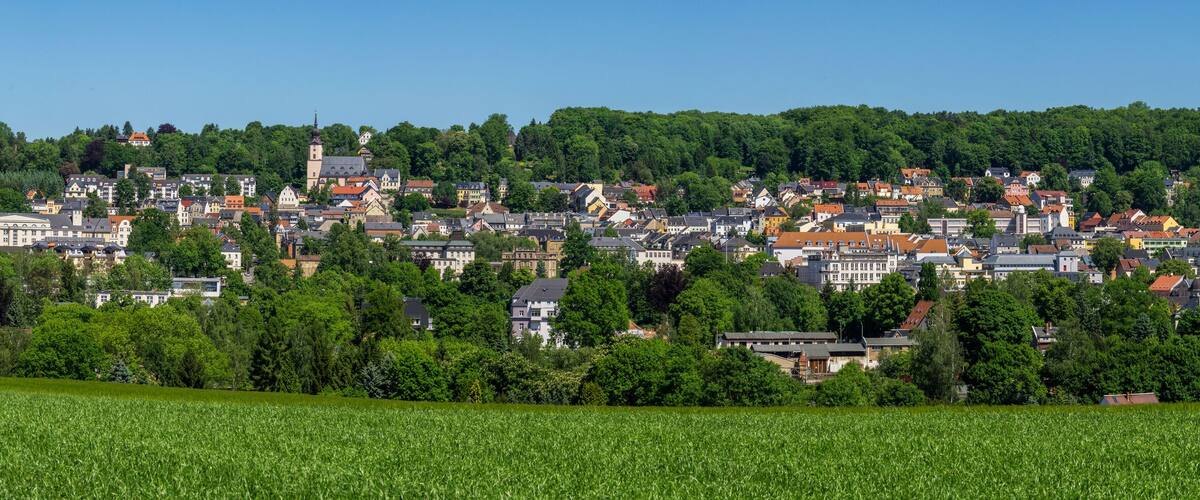 A town nestled in a valley with a prominent church tower, surrounded by lush greenery and fields.