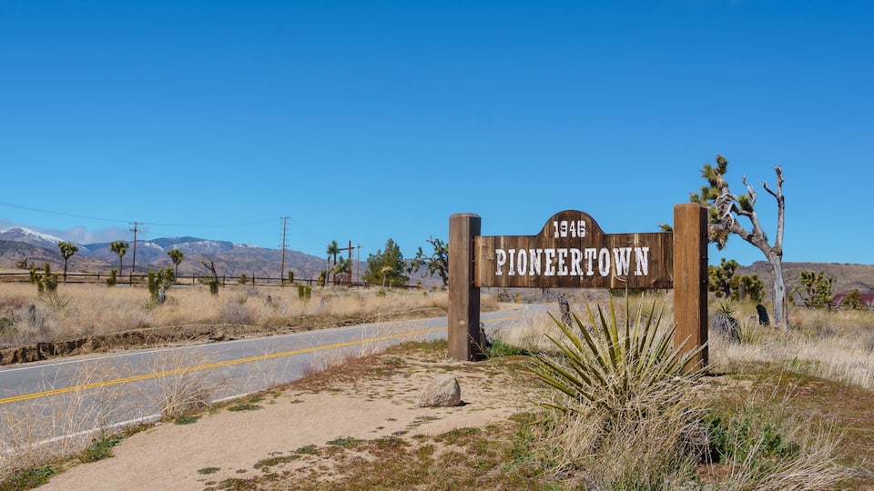 A wooden sign with '1945 PIONEERTOWN' written on it, surrounded by desert vegetation and a clear blue sky.