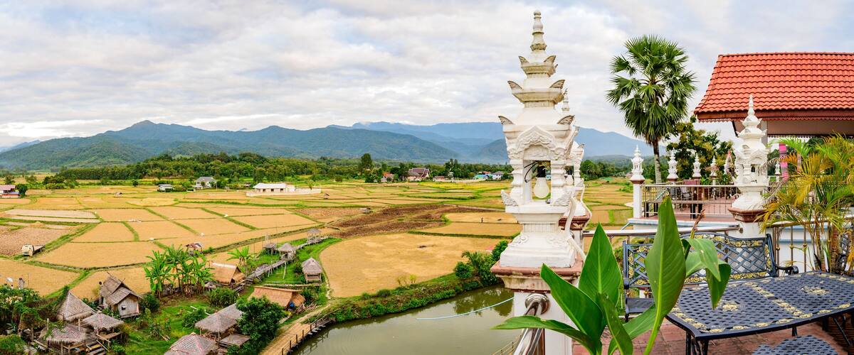 A rural landscape with terraced rice fields, a white stupa, and mountains in the background.