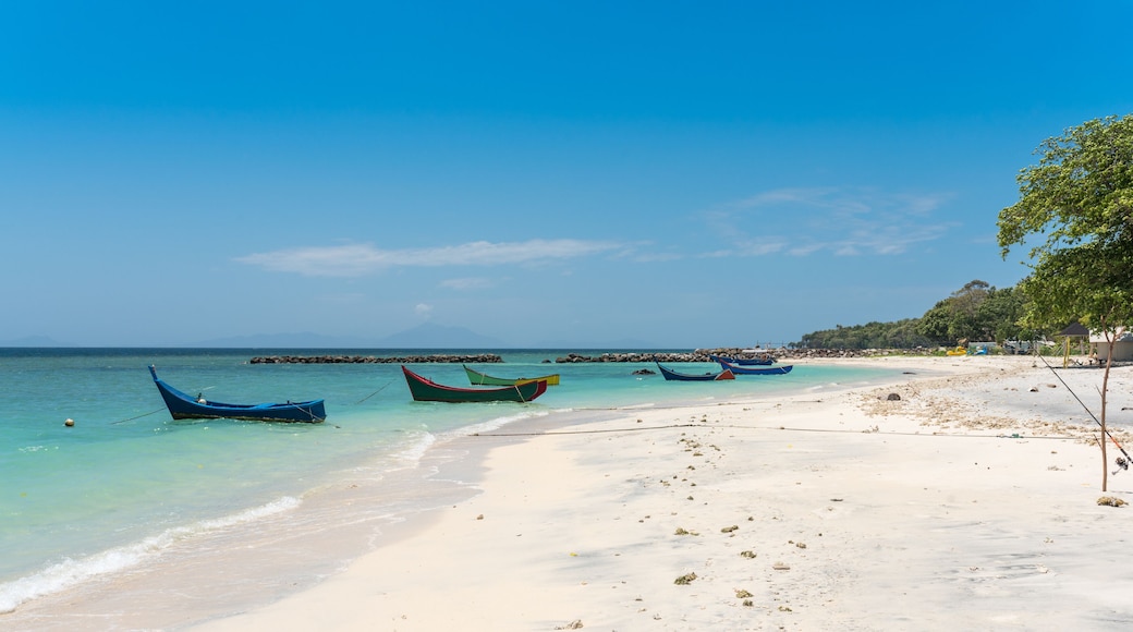 A beach with several boats anchored near the shore, clear turquoise water, and a sandy beach.