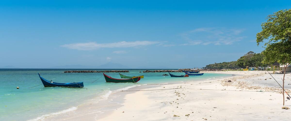 A beach with several boats anchored near the shore, clear turquoise water, and a sandy beach.