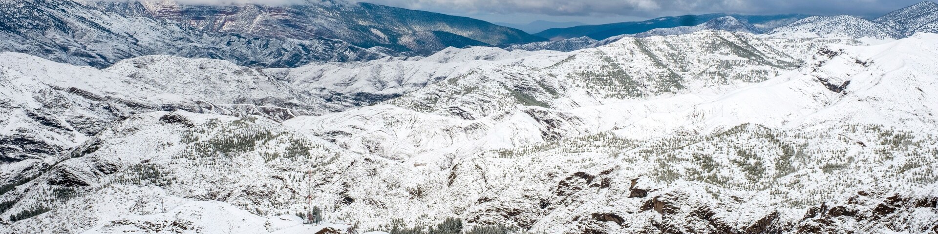 Paisagem montanhosa coberta de neve, com estradas sinuosas e nuvens ao longe.