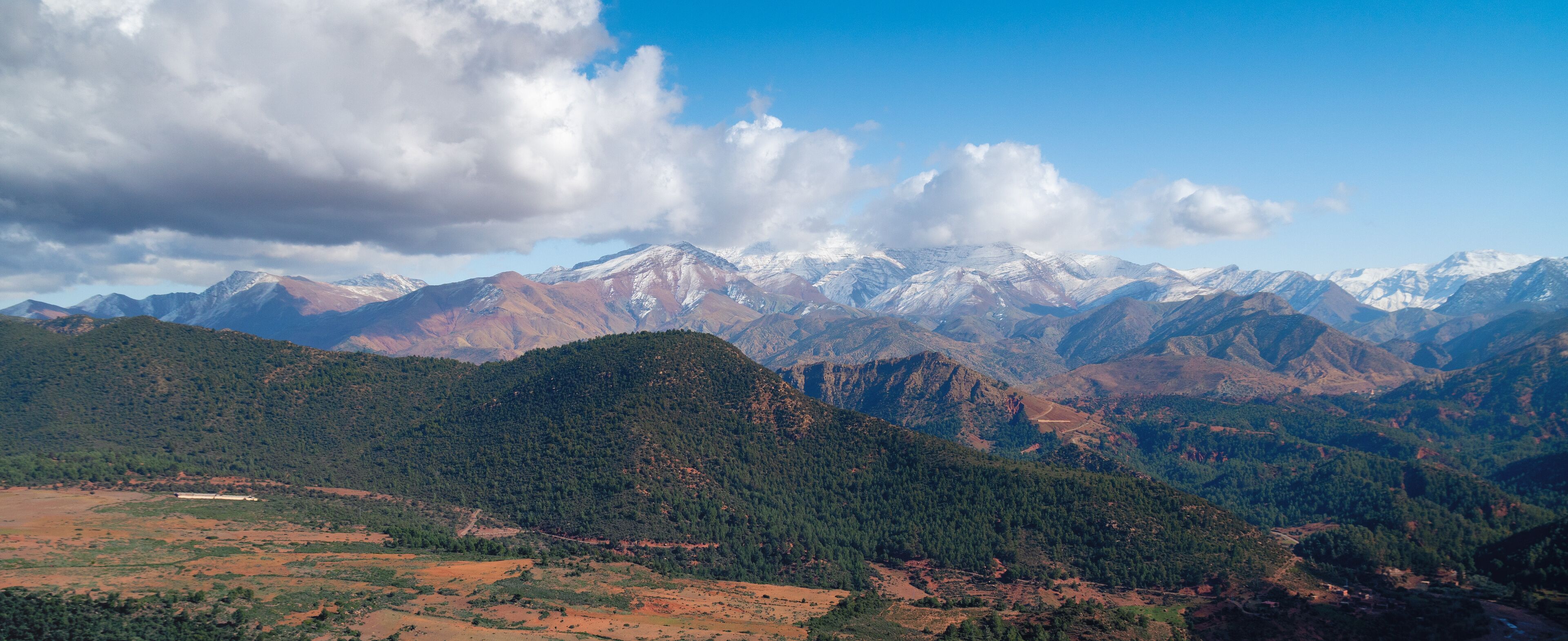 A mountainous landscape with snow-capped peaks, dense forests, and a clear sky.