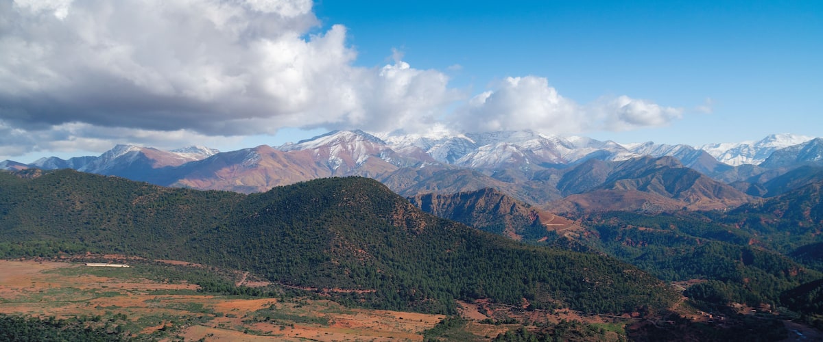 A mountainous landscape with snow-capped peaks, dense forests, and a clear sky.