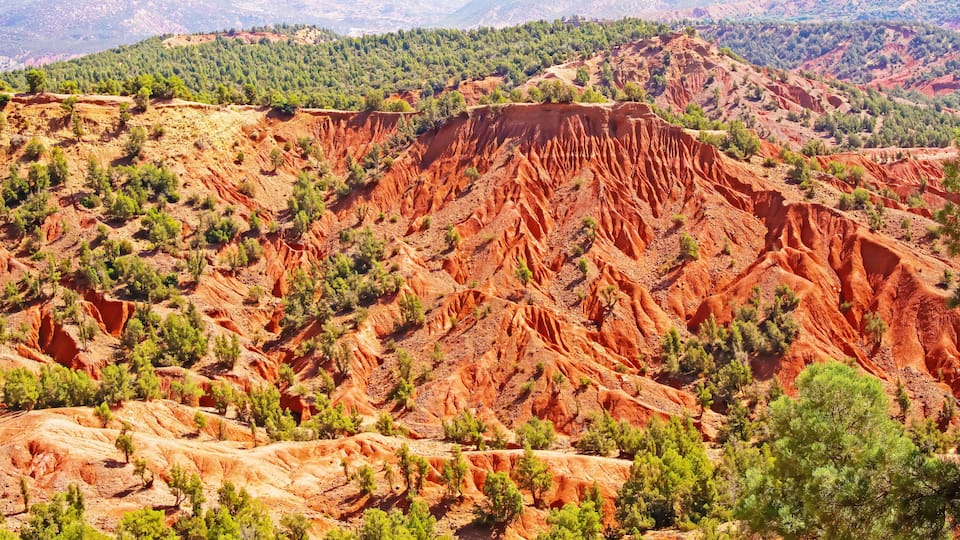 A rugged landscape with red rock formations, green vegetation, and distant hills.