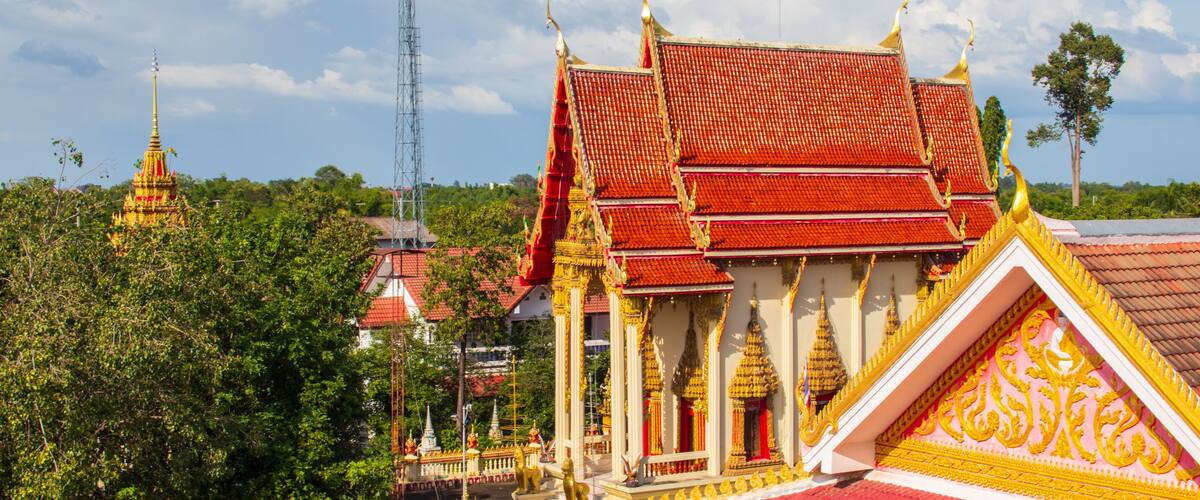 A temple with a red roof and golden decorations, surrounded by trees and a clear sky.