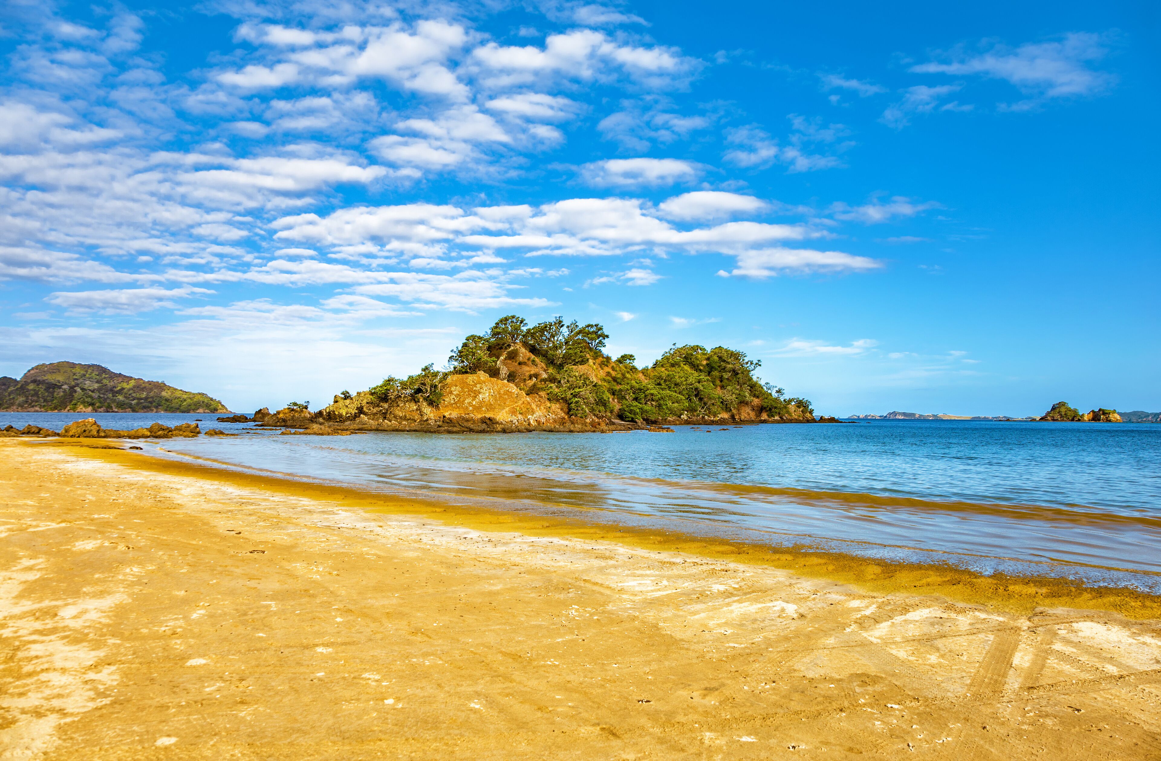 A sandy beach with clear blue water and a small island with trees in the distance.
