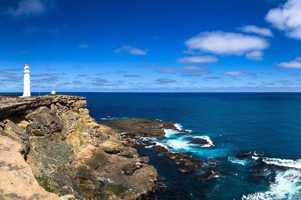 Un faro blanco sobre un risco con vista al océano.