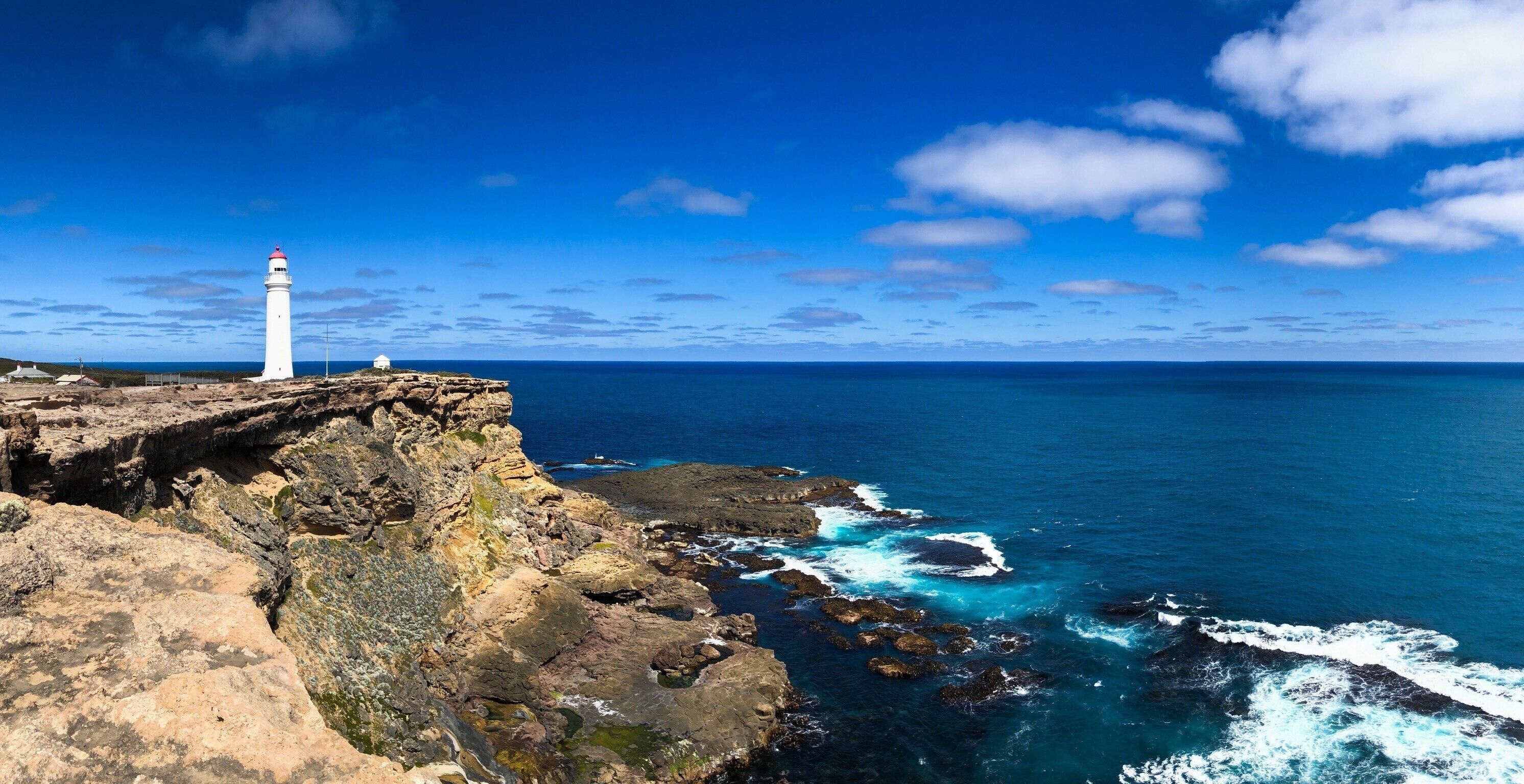 A white lighthouse on a rocky cliff overlooking the ocean.
