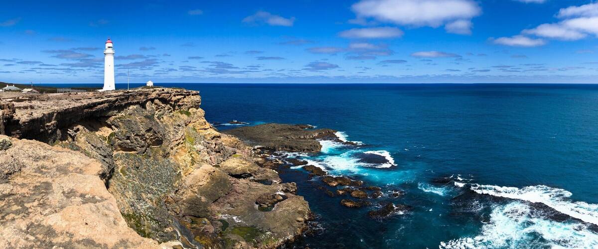 A white lighthouse on a rocky cliff overlooking the ocean.