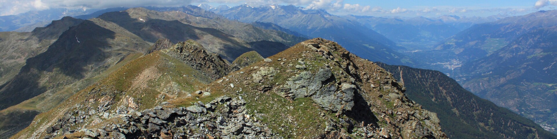 Auf dem Gipfel der Naturnser Hochwart (2608 m.ü.M.). Der Blick geht hier auf dem Gipfelkamm in Richtung Westen ins Ortlergebiet. Rechts unten liegt der Vinschgau. Die Naturnser Hochwart (italienisch Guardia Alta) ist ein 2608 Meter hoher Berg im Zufrittkamm der Ortler-Alpen. Die Hochwart befindet sich im italienischen Südtirol und trennt die Vinschger Gemeinde Naturns von der Ultner St. Pankraz.