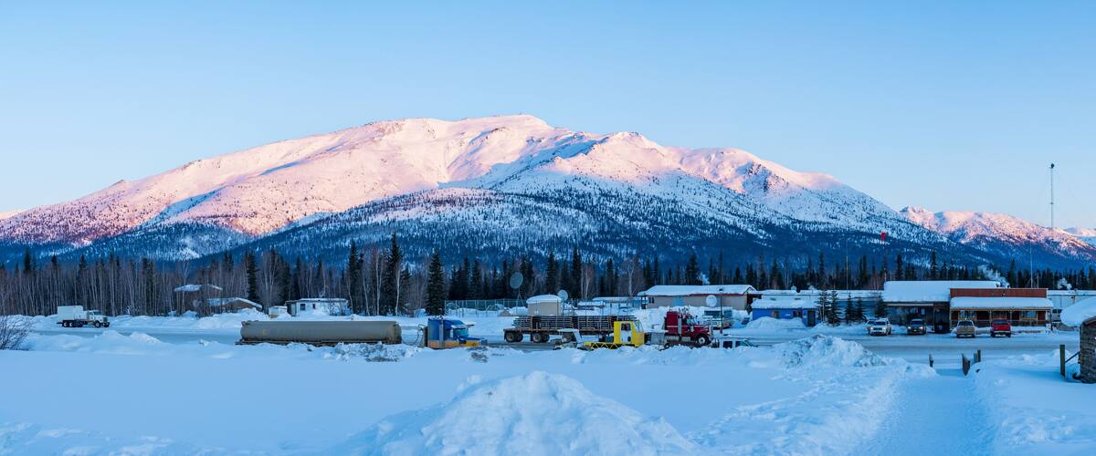 A snowy mountain landscape with a small settlement and several trucks.