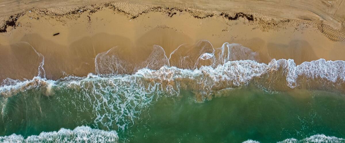 A beach with clear turquoise water, a sandy shore, and a distinct line of seaweed or debris in the water.