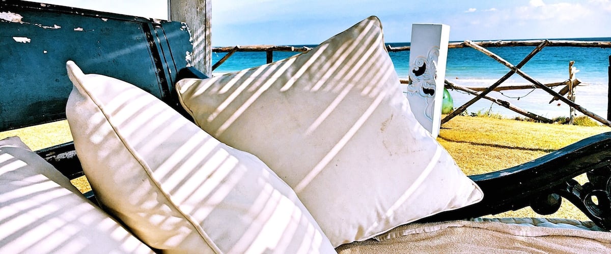 A beach chair with white cushions and a wooden structure in the background.