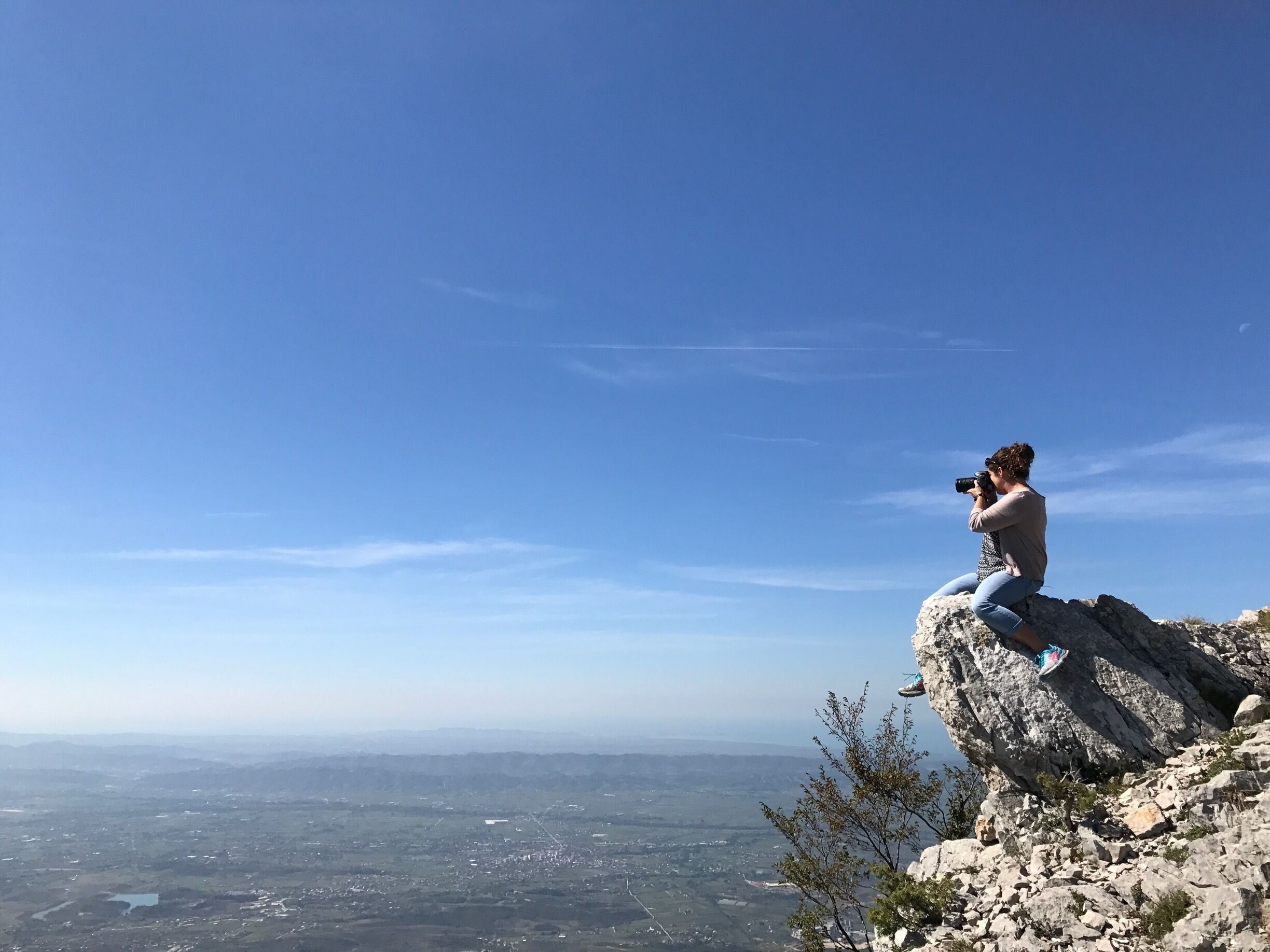 A person taking a photo on a rocky cliff overlooking a valley.