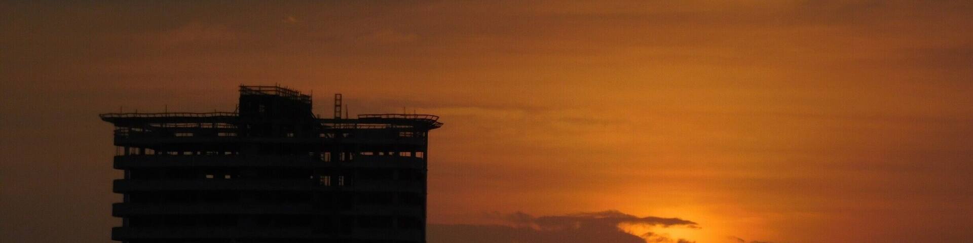A sunset with a silhouette of a tall building against a sky with clouds.