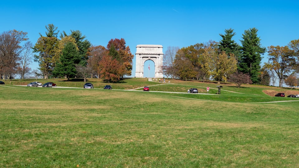 A grassy hill with a monument, trees, and parked cars.