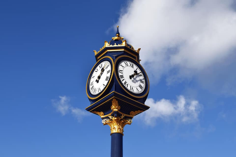Una alta torre del reloj con dos esferas, sobre un cielo azul despejado.