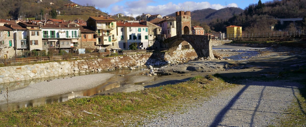 A stone bridge over a river, surrounded by historic buildings and a mountainous backdrop.