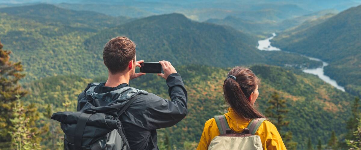 Two people taking a photo of a river winding through a mountainous landscape.