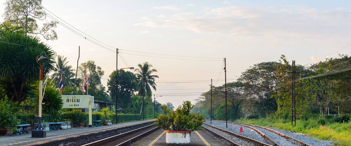 A railway platform with tracks, a planter with greenery, and a sign with text.