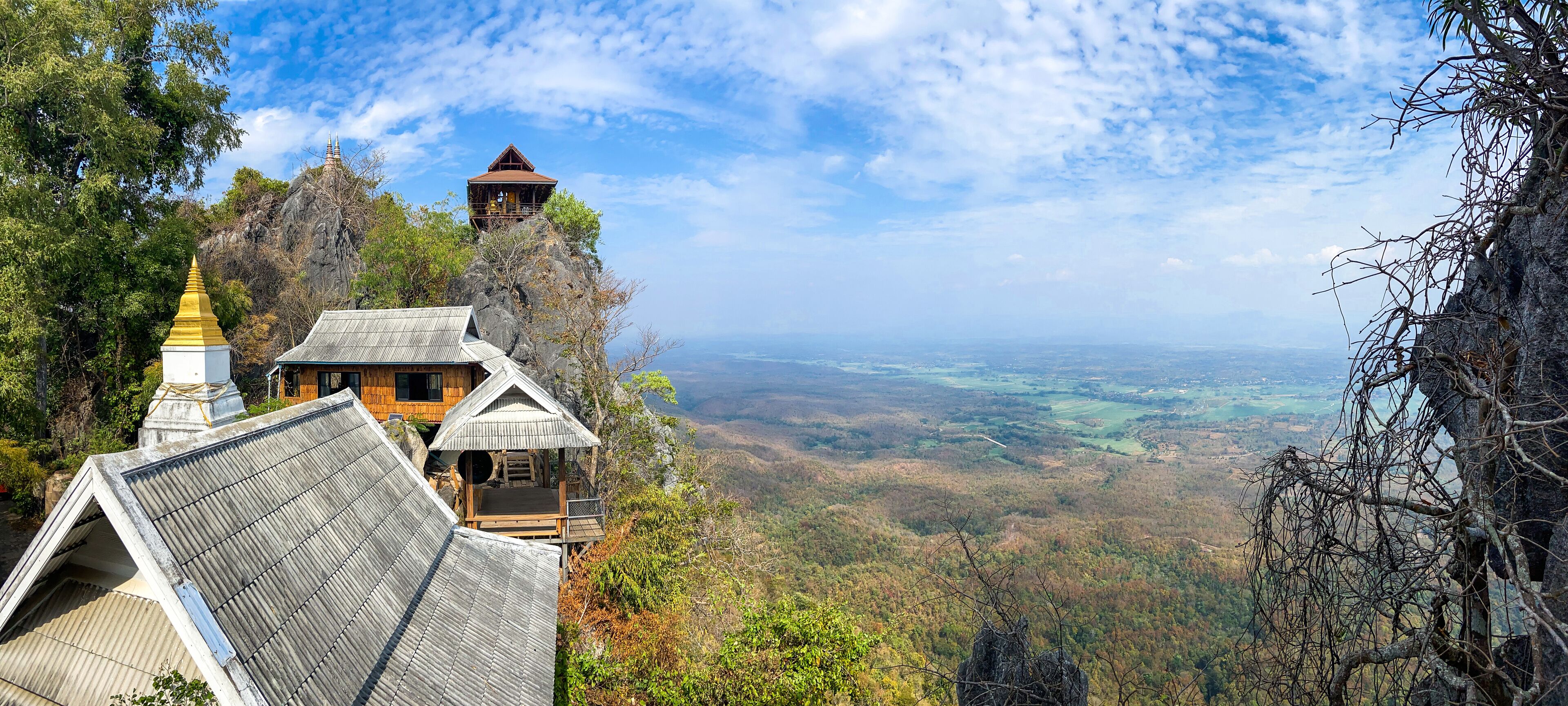 A wooden house with a thatched roof on a hillside, overlooking a valley.
