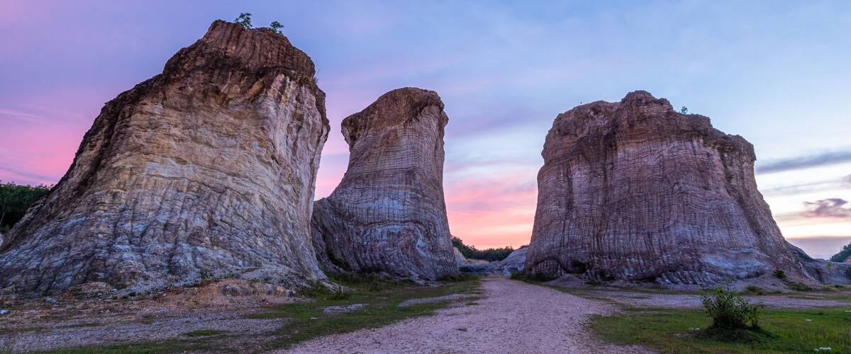 A gravel path leading to three large rock formations with a sunset sky.