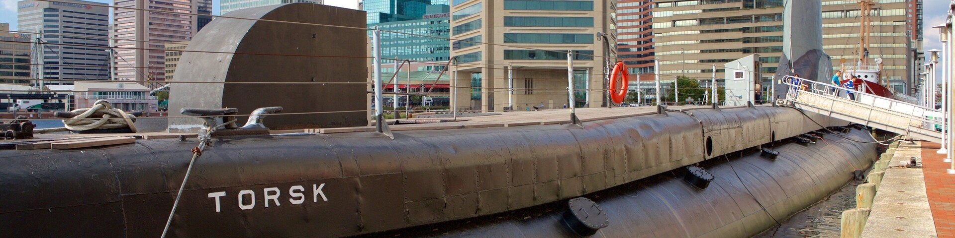Um submarino grande atracado em um cais, com um horizonte urbano ao fundo.