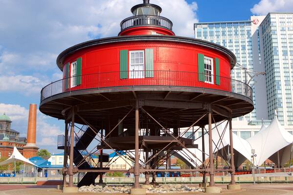A red lighthouse with green shutters, a historic building, and modern skyscrapers in the background.