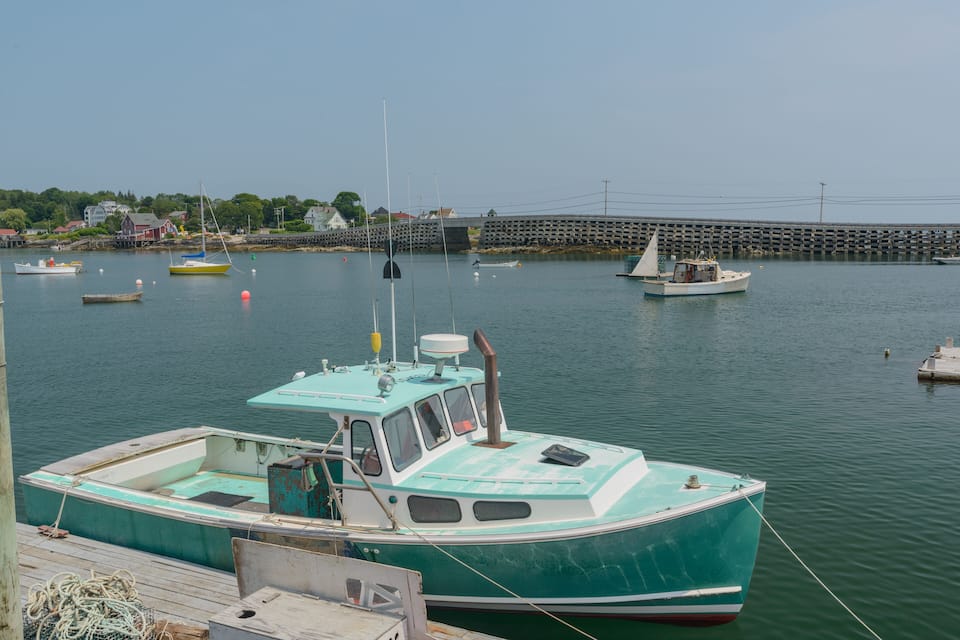 A harbor with several boats docked, a pier, and a bridge in the background.