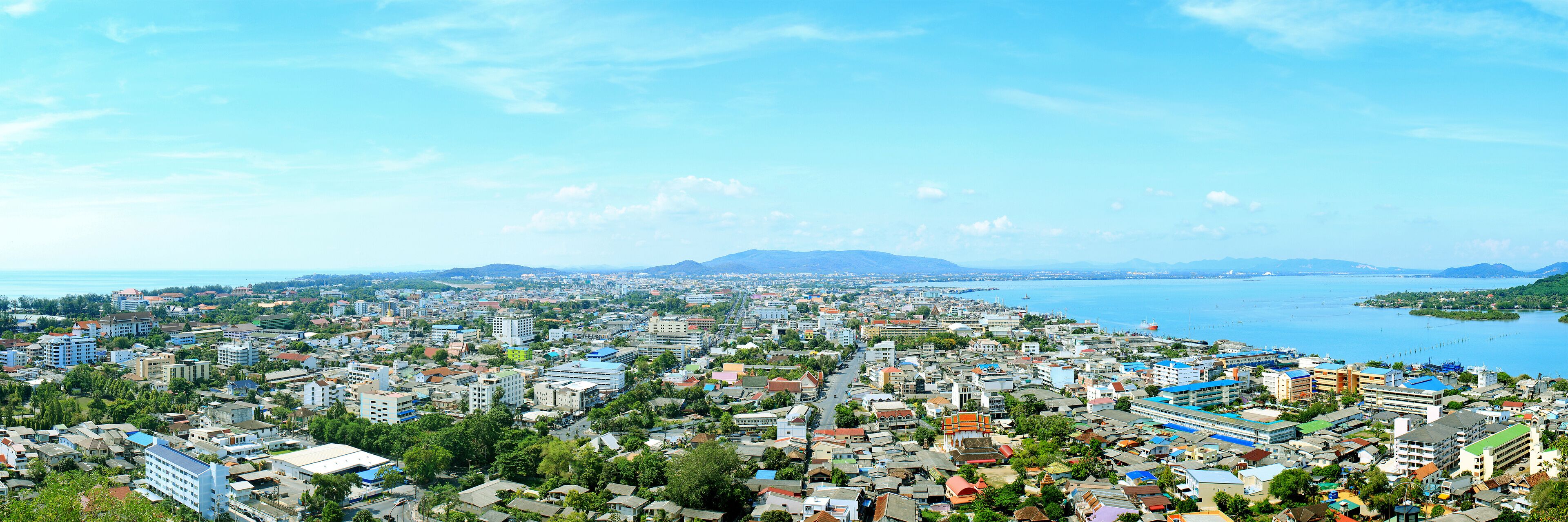 A coastal cityscape with dense urban buildings, a harbor, and distant mountains.