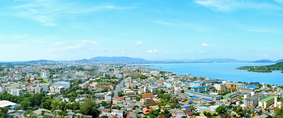 A coastal cityscape with dense urban buildings, a harbor, and distant mountains.