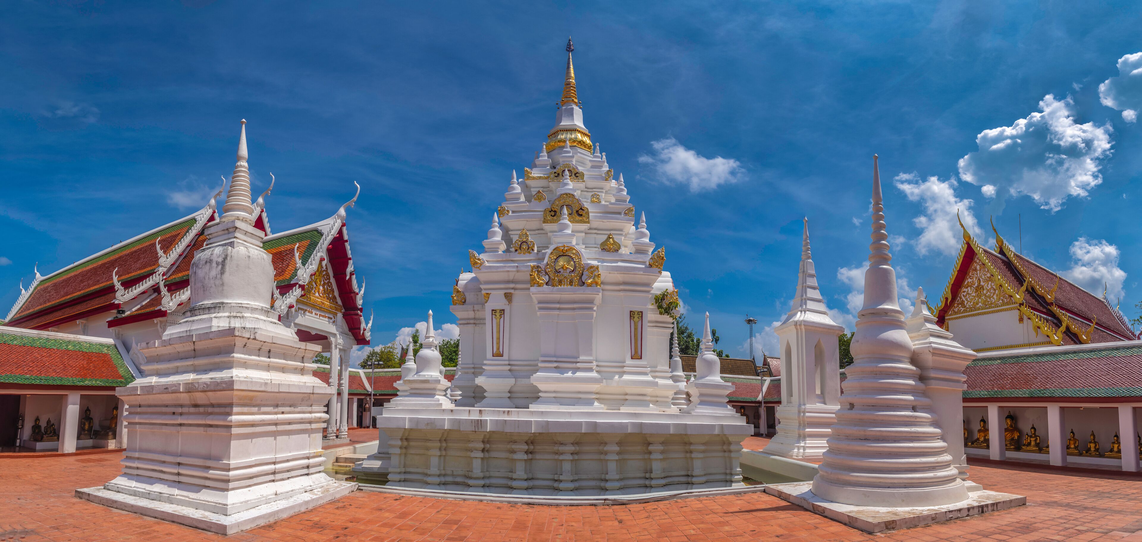 A white temple with a golden spire, surrounded by smaller white structures with red and green roofs.