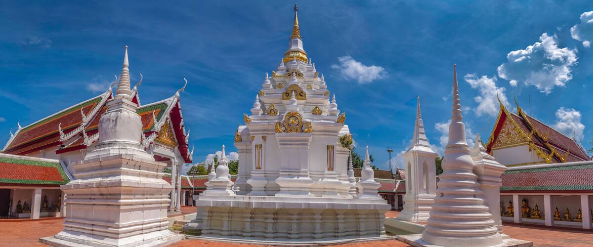 A white temple with a golden spire, surrounded by smaller white structures with red and green roofs.