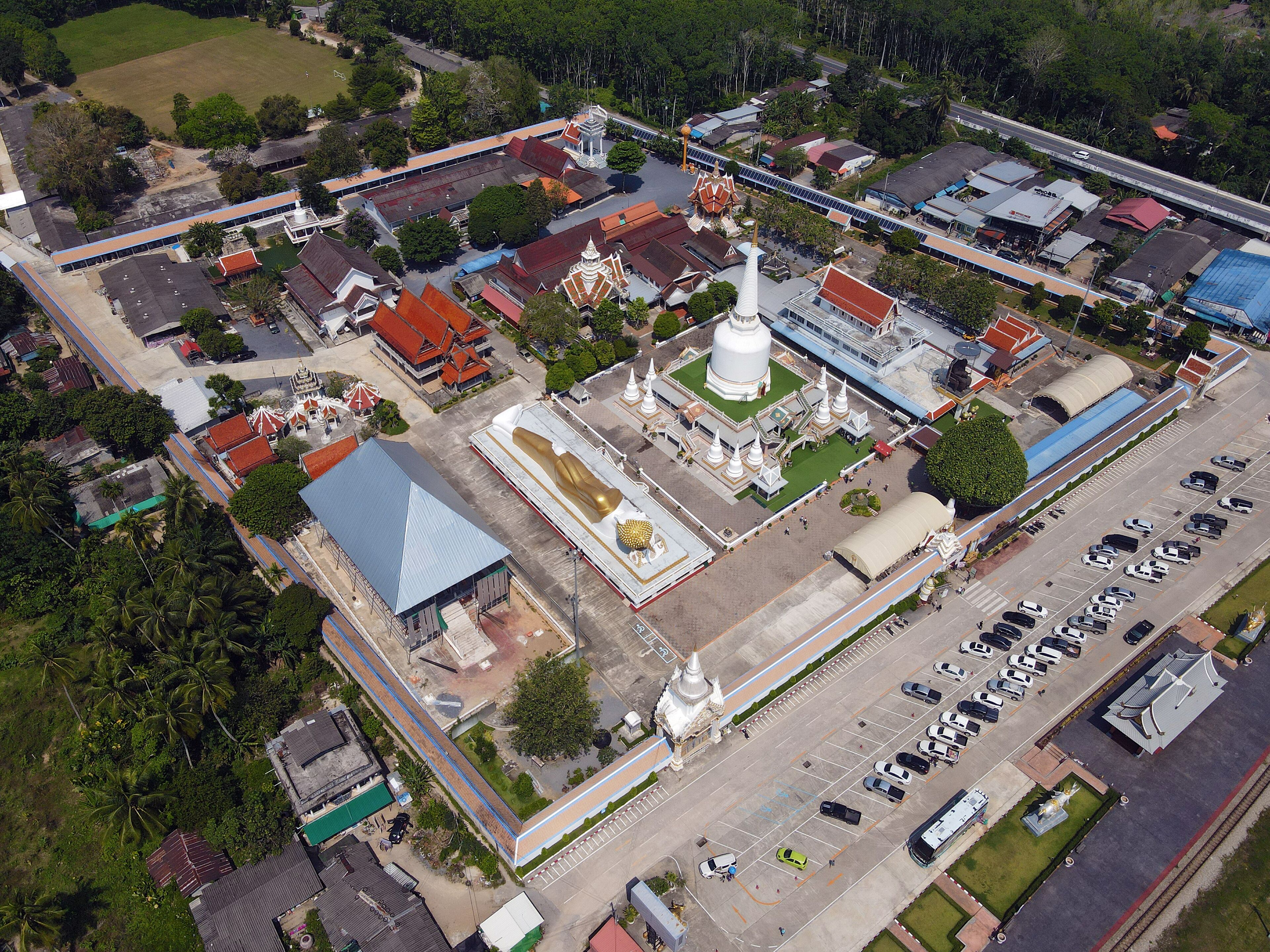 An aerial view of a temple complex with a large golden statue, surrounded by smaller structures and a parking lot.