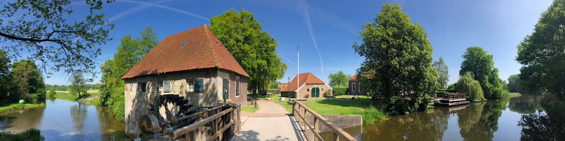 A riverside scene with a water mill, a wooden bridge, and a small brick building.